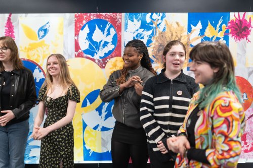 A group of young artists standing and smiling in front of an artwork they created