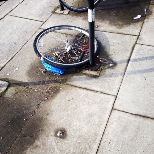 Picture of a single bike wheel locked to a post on the pavement, the rest of the bike presumably stolen.