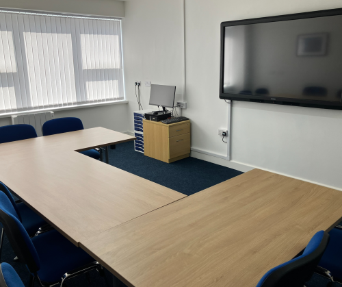 An image of our community room -- pictured is a desk in a U formation and a presenting space equipped with an interactive whiteboard.