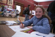 Child smiling while colouring in, sitting in an art gallery