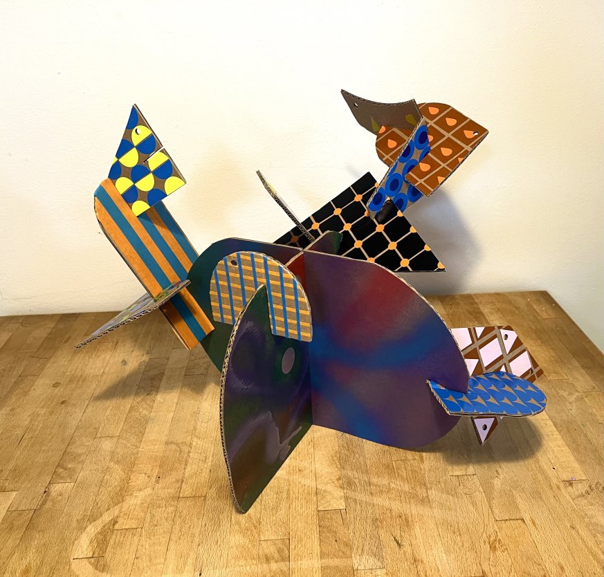 A sculpture made out of varying coloured and patterned cardboard.