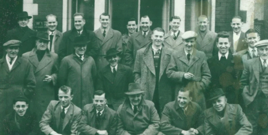 an old black and white photo of a groups of men in three rows, smiling for the camera