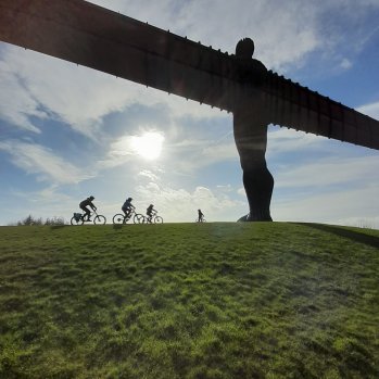 The Angel of the North, pictured with the sun behind it and cyclists on the horizon