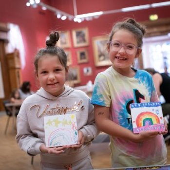 Two children in a gallery showing their art work to the camera