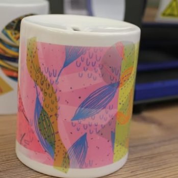 White ceramic cylinder money box with pink and blue abstract pattern.