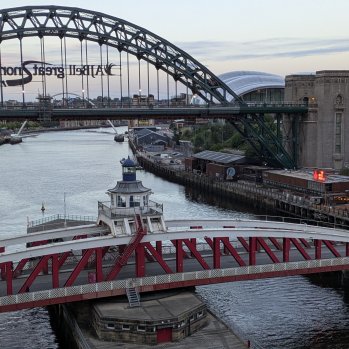 Two bridges cross a wide river - one is the high arch of the Tyne Bridge, and the other is the red-painted low-level bridge