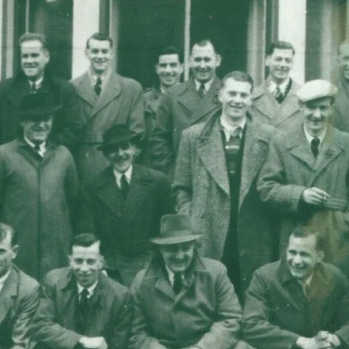 an old black and white photo of a groups of men in three rows, smiling for the camera