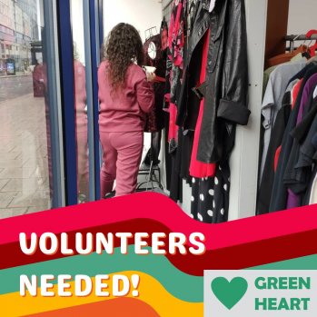 person in shop window, text graphic says "volunteers needed" at GREEN HEART
