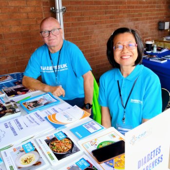 Two volunteers in Diabetes UK blue t shirts hosting an information stand at a community event.