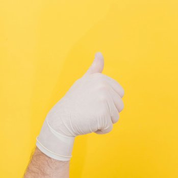 Hand in rubber glove showing the thumbs up against a yellow background
