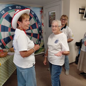 Older women playing darts in front of a large fabric darts board