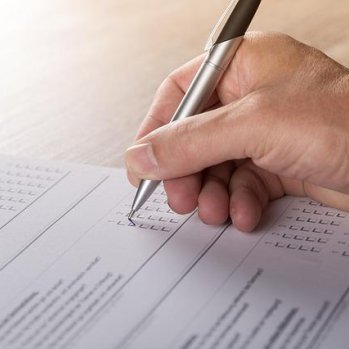 photo of someone hand, holding a pen filling in a survey