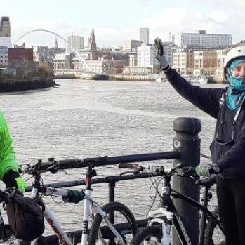 Two riders waving by their bikes on the quayside
